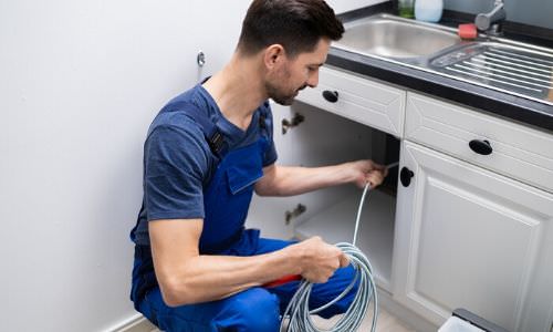 plumber snaking pipes under sink
